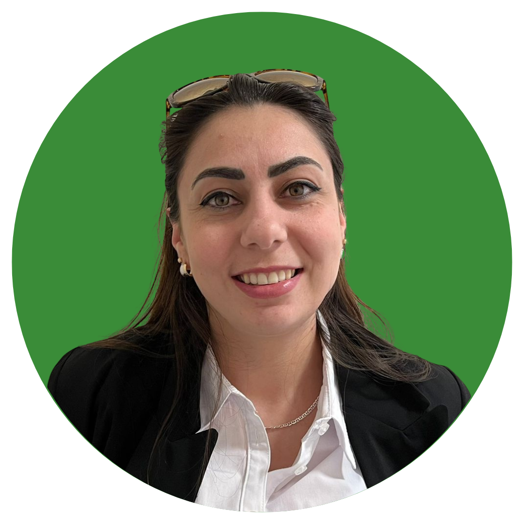 A woman with long dark hair smiles at the camera. She is wearing a black blazer with a white shirt, and wears sunglasses on her head. She is set against a dark green background.