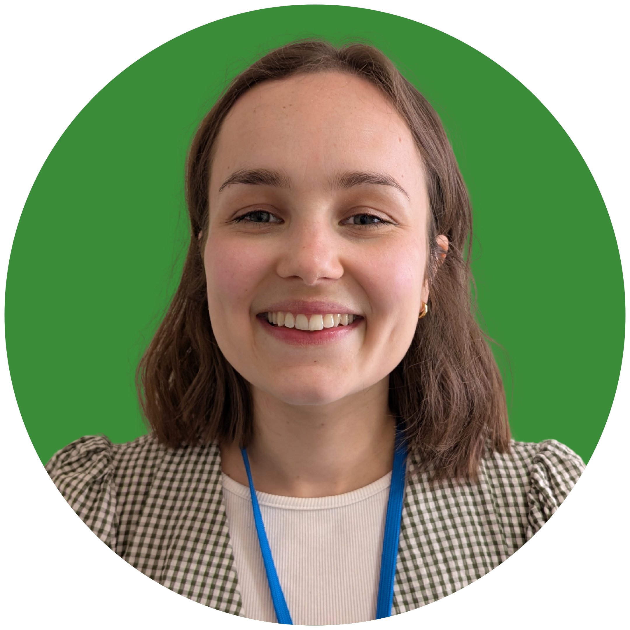 A brown-haired, olive-skinned woman smiles at the camera. She is wearing a green checked shirt, and is set against a green background.