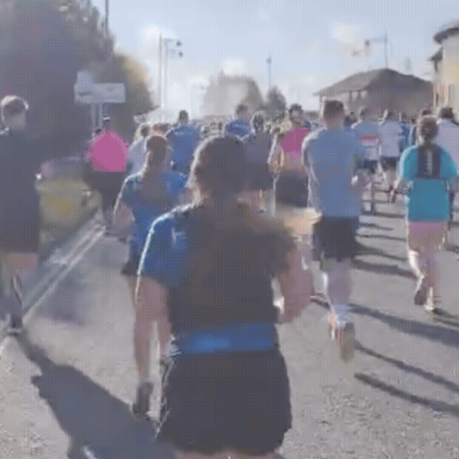 GIF shows a crowd of people running through Pride Park in Derby. The text written over it says: Derby Half Marathon, 28.06.26