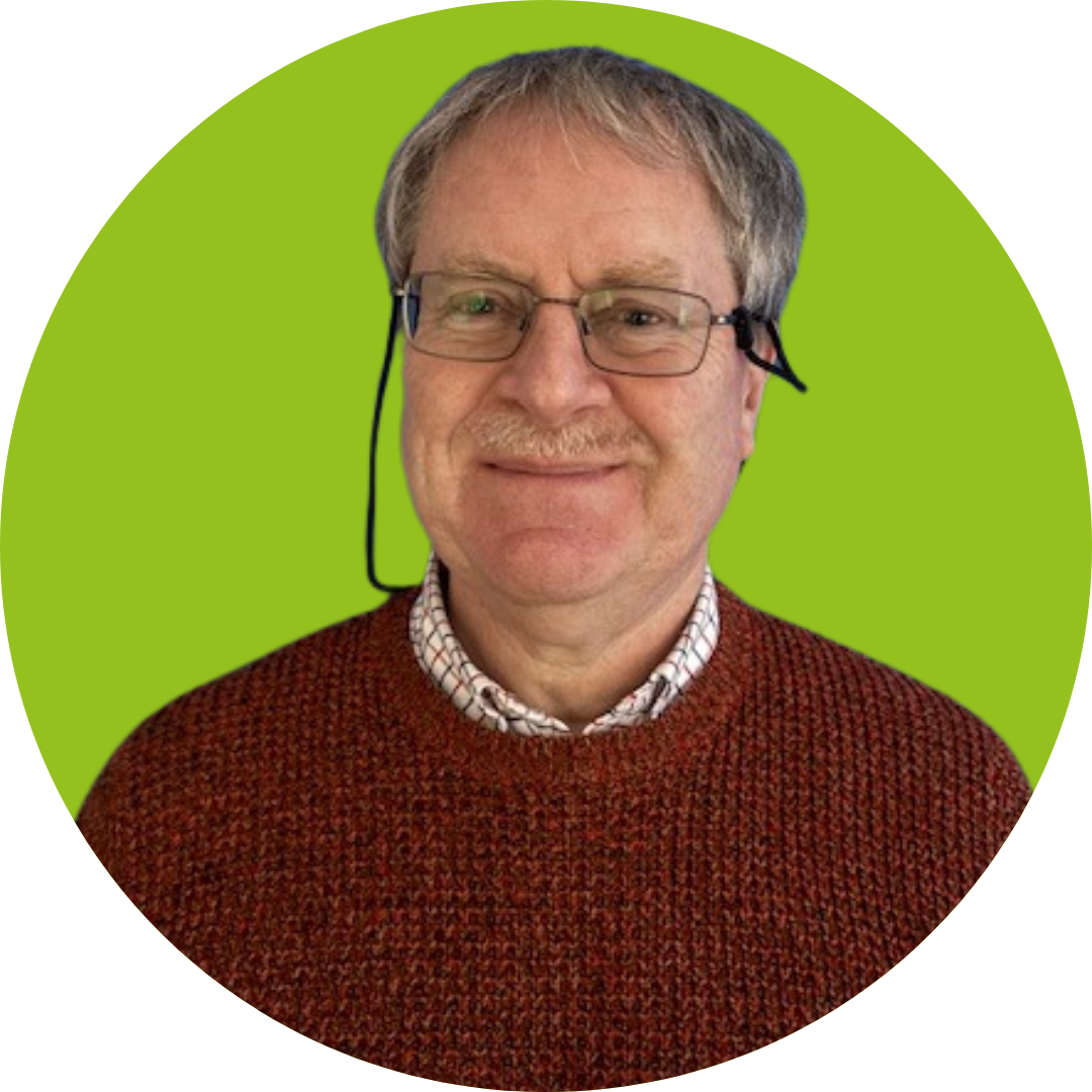 A man with grey hair and a moustache smiles at the camera. He is wearing glasses and a red jumper. He is set against a light green background.