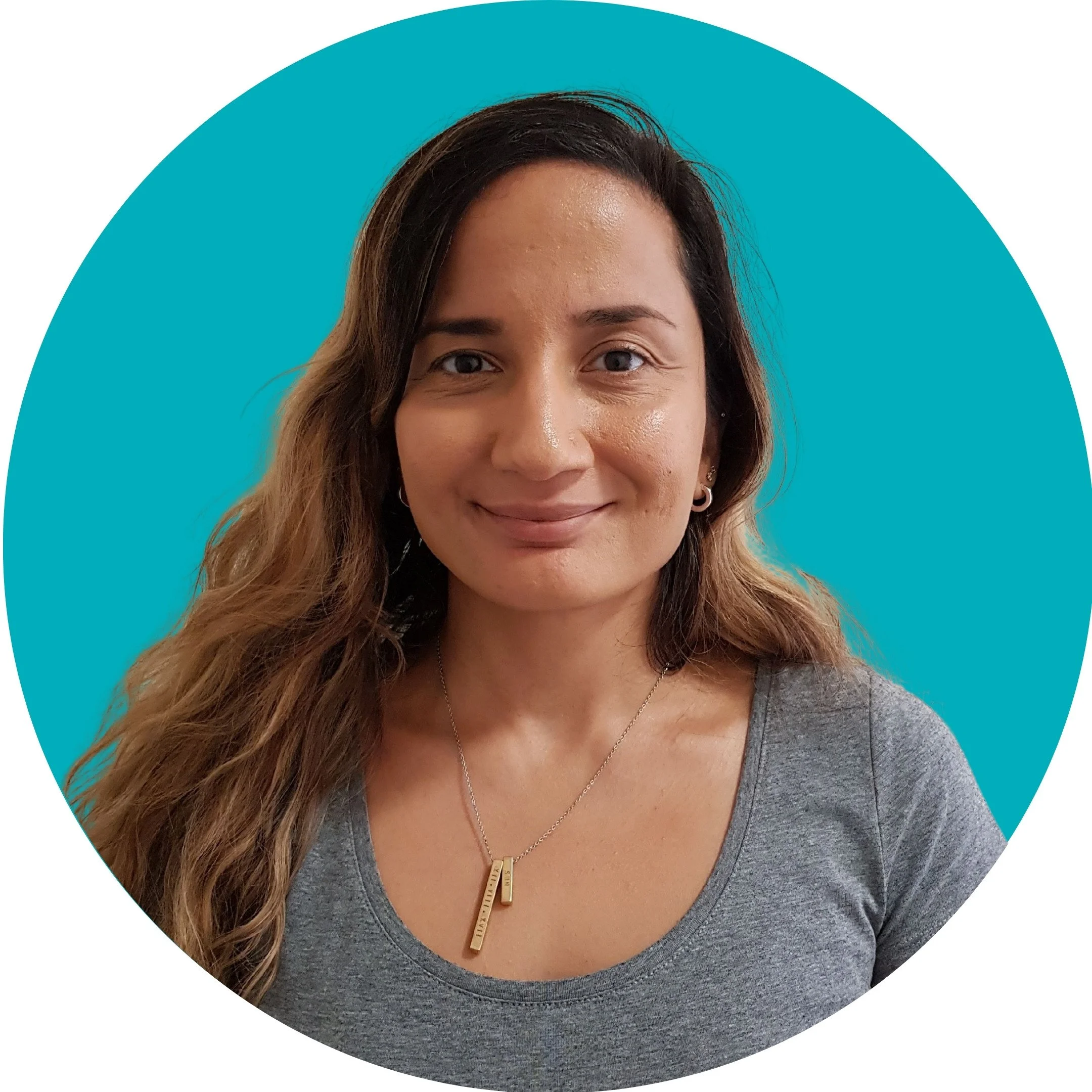 A woman with long dark hair smiles at the camera. She is wearing a grey T Shirt and set against a teal background.