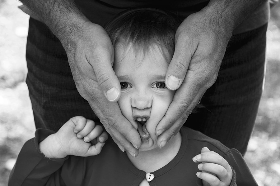 Black and white portrait of young child's face sqished in dad's hands.jpg