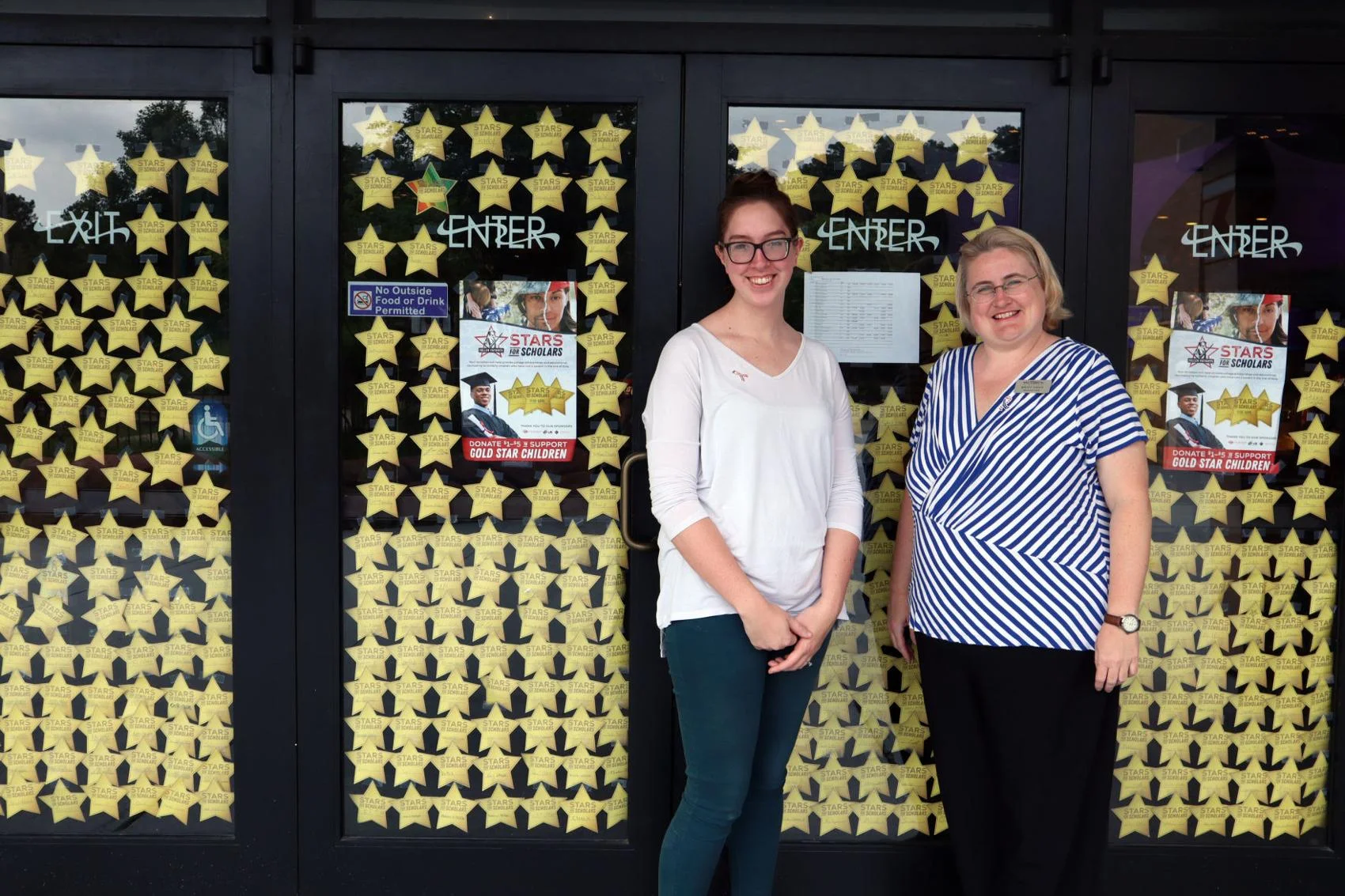 From left, Rachel Eisenbrandt and Britt Argo, stand in front of the ‘Stars for Scholars’ sign posted on the doors of Aurora Cineplex in Roswell. Both Eisenbrandt and Argo, who work at the theatre, have family members who served in the armed forces. Lindsay Moscarello