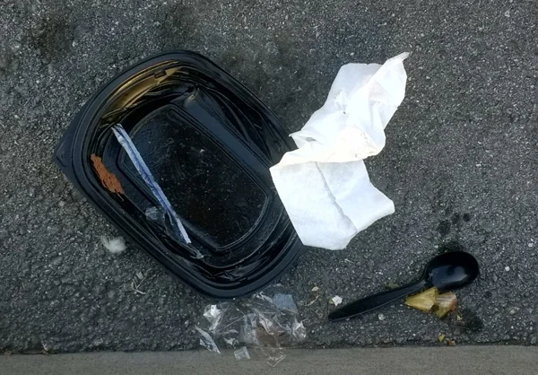 Black plastic take-out tray, black plastic spoon, and cellophane in the street.