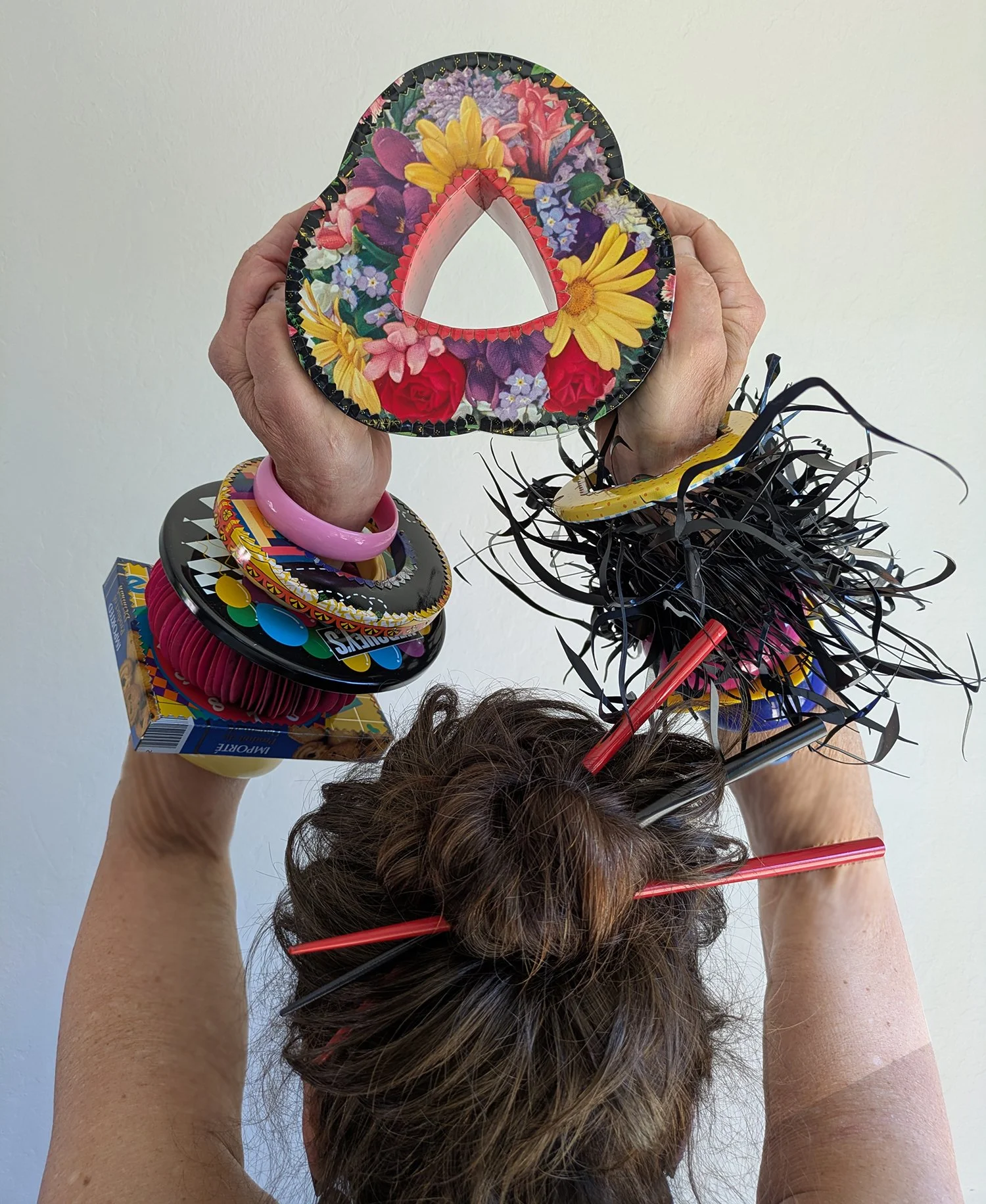 Artist Harriete Estel Berman holding a Wrist Coursage Bracelet overhead while wearing bracelets