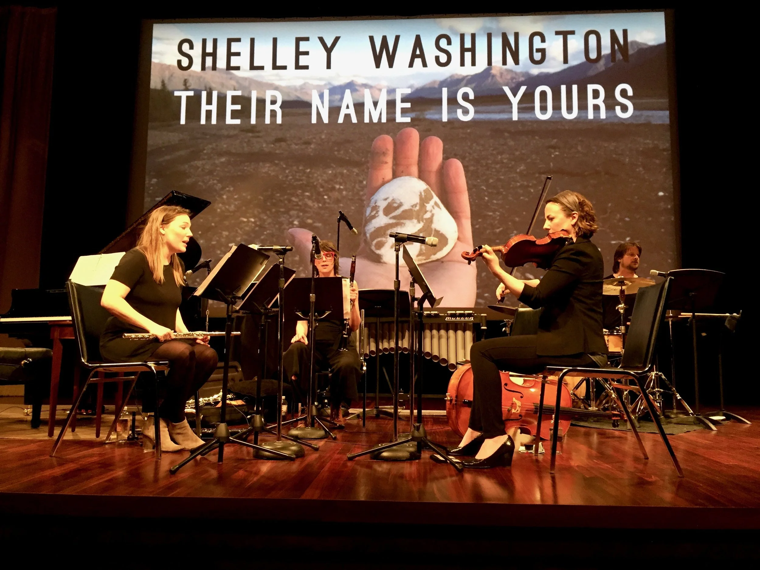 Musicians and leaders of Wild Shore New Music , Katie Cox playing flute (left), Andie Tanning Springer on fiddle (right), with Christa Van Alstine on clarinet (center) and Michael McCurdy on drum set (far right) performing "Their Name Is Yours" at the U.S. National Archives on March 30th, 2017.