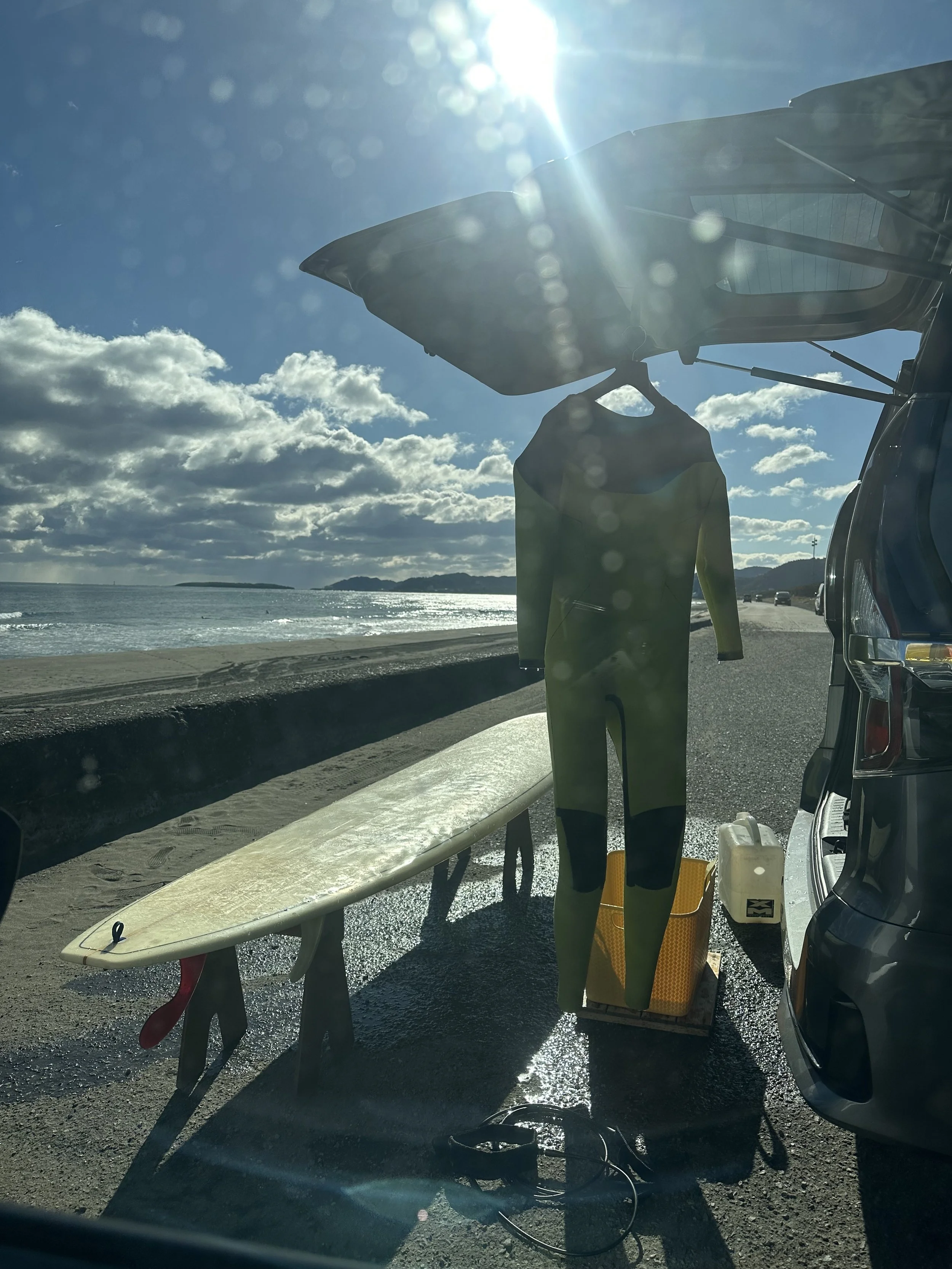 surfboard and wetsuit next to a van