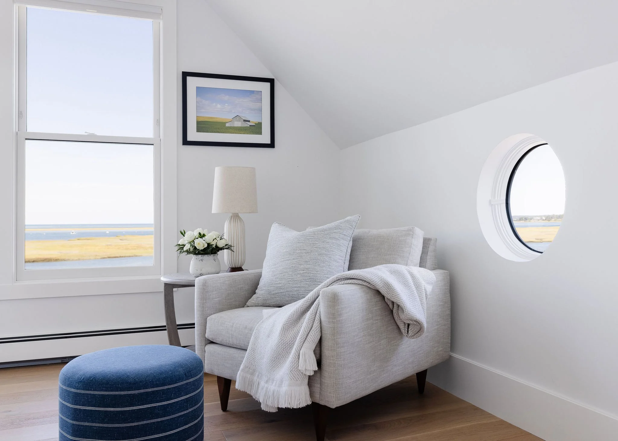White room with rectangular and square windows, and a low-back loveseat with a deep blue and white stripped ottoman.