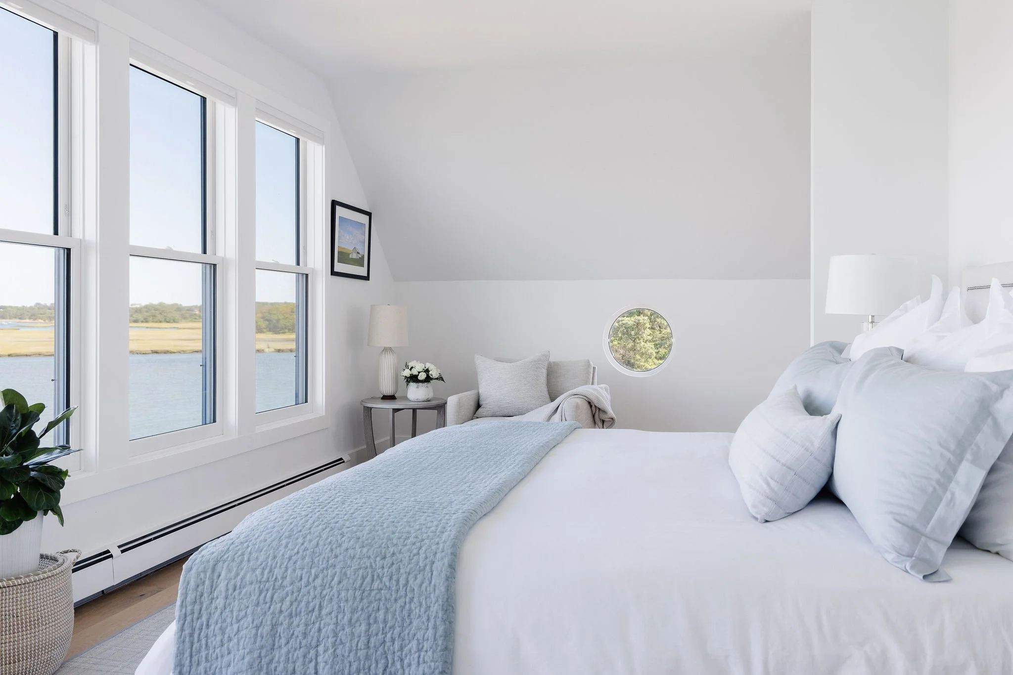 White bedroom with an angled ceiling, 3 windows, and a bed with a powder blue throw blanket.