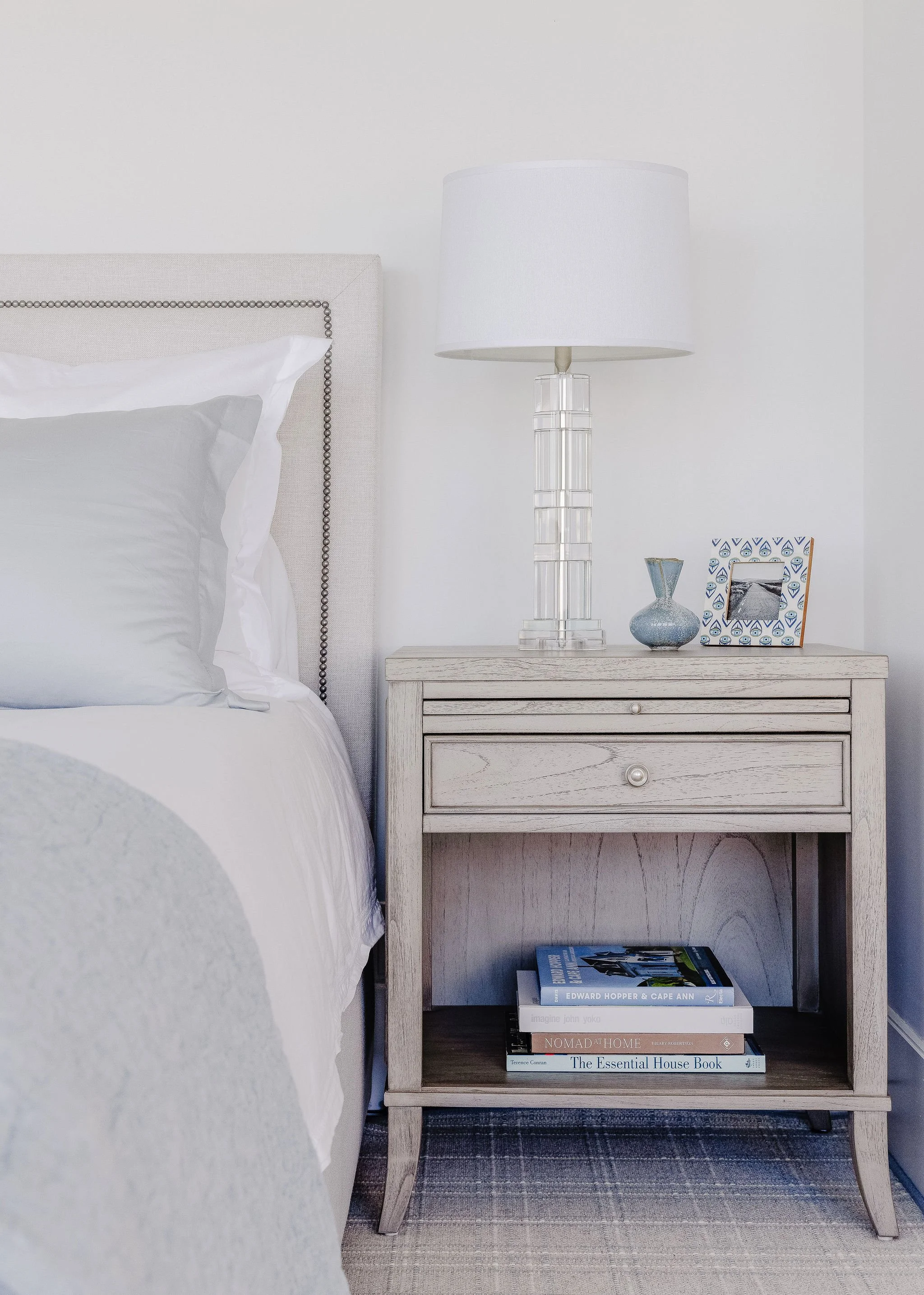 Bed with a cream colored upholstered headboard next to a light brown wooden nightstand.