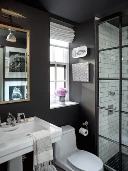 Black walls, shower door hardware, and shower floor tile make this bathroom a complete stunner. Image via Traditional Home