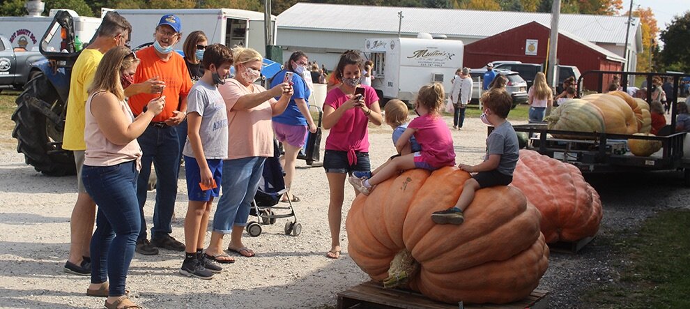   9th Annual Gouverneur Pumpkin Fest attendees enjoying taking photos as local youth sit atop the second heaviest pumpkin entered into the weigh-off contest. (Rachel Hunter photo)  
