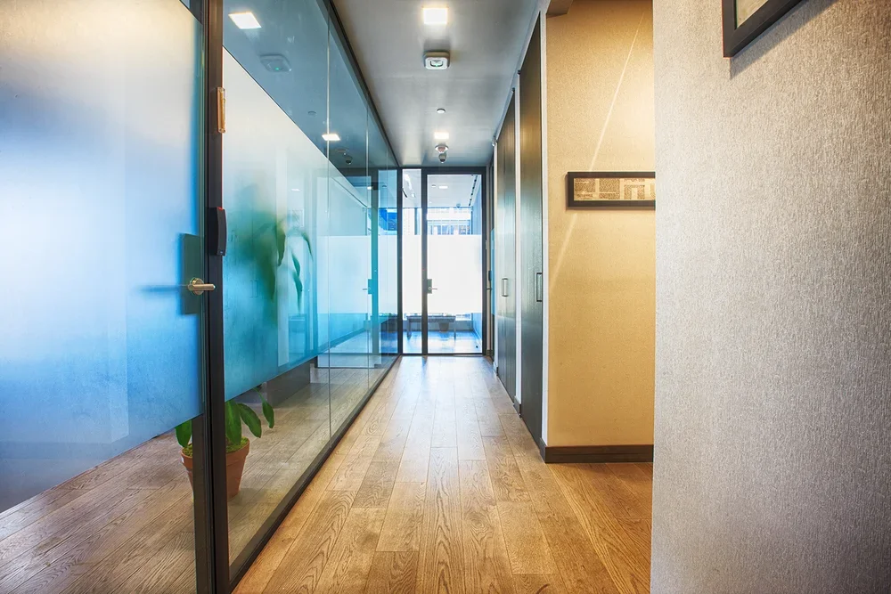 Hallway with wooden floor, frosted glass walls, and glass door at the end, with framed pictures on the walls.