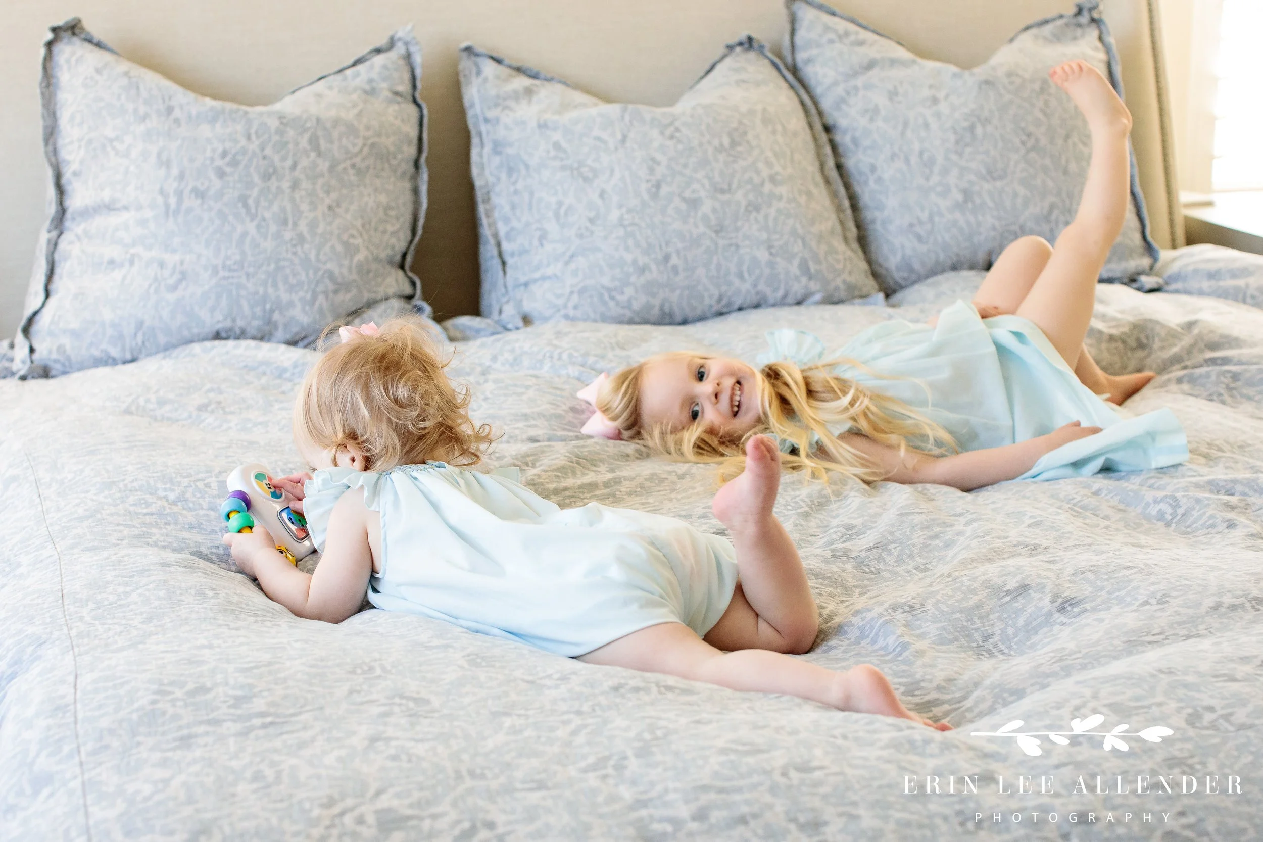 Two sisters playing and laughing on parents’ bed, in-home Nashville family photography