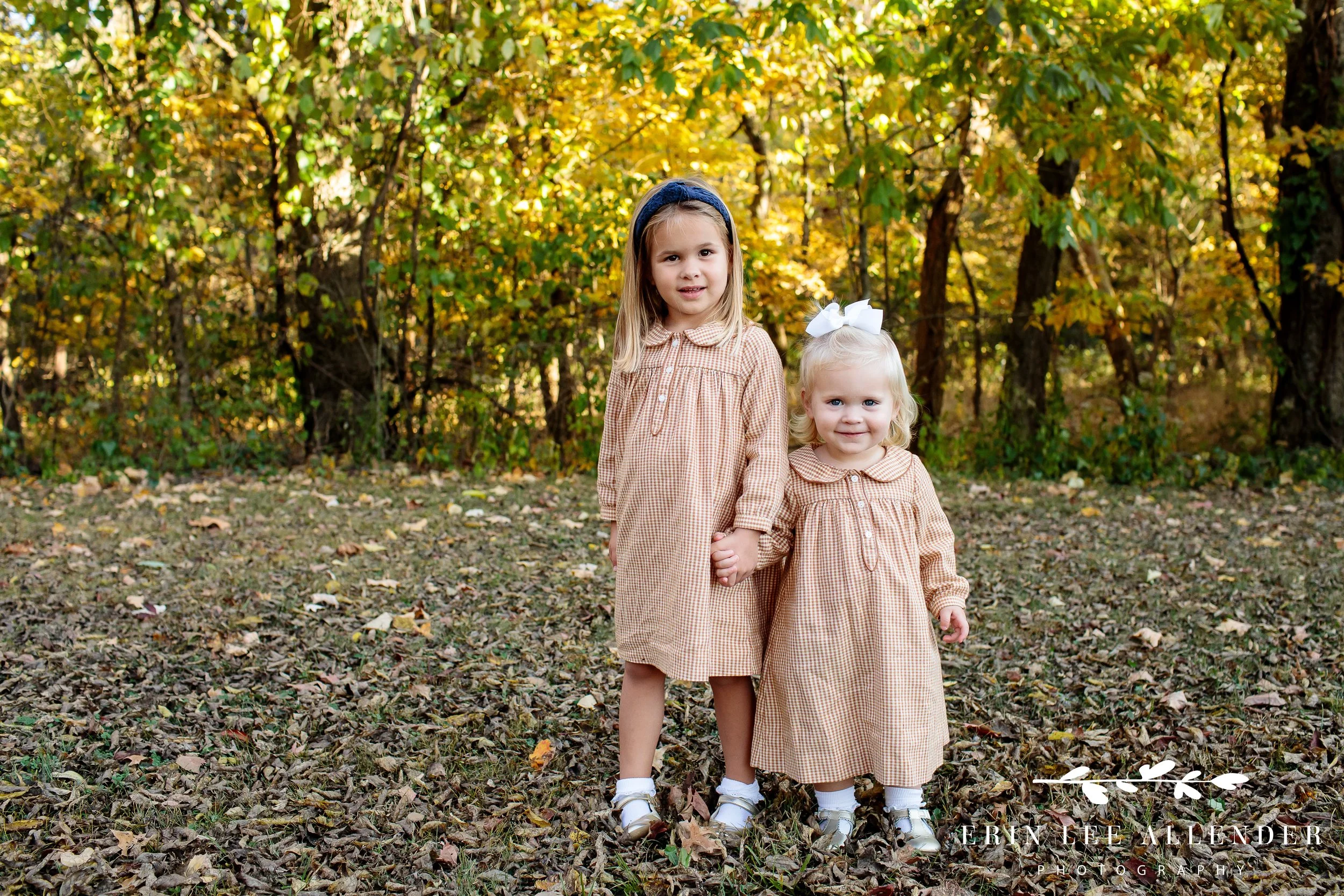 Sisters in matching gingham dresses holding hands on a fall path with colorful leaves in Nashville family portraits.