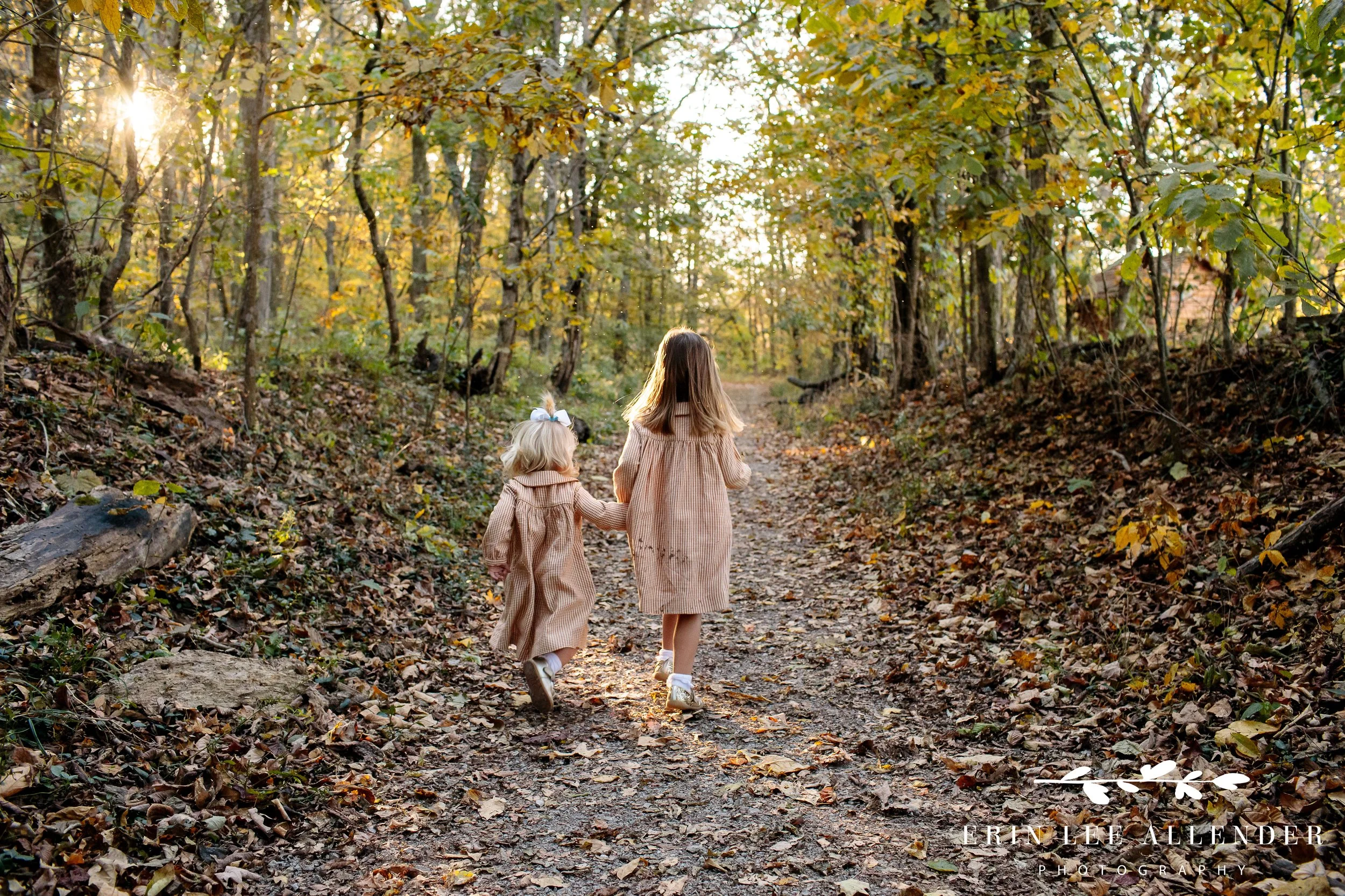 Sisters walking hand in hand down a wooded path with fall leaves during Nashville family photography session.