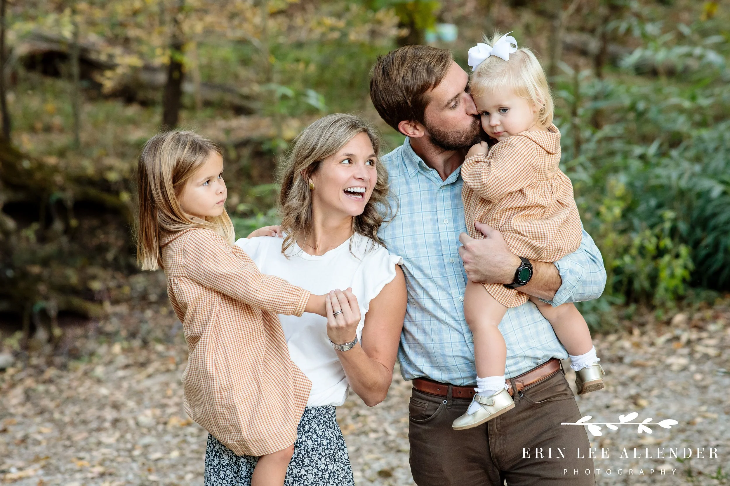 Father kissing his toddler daughter as mother smiles during candid Nashville family photography session.