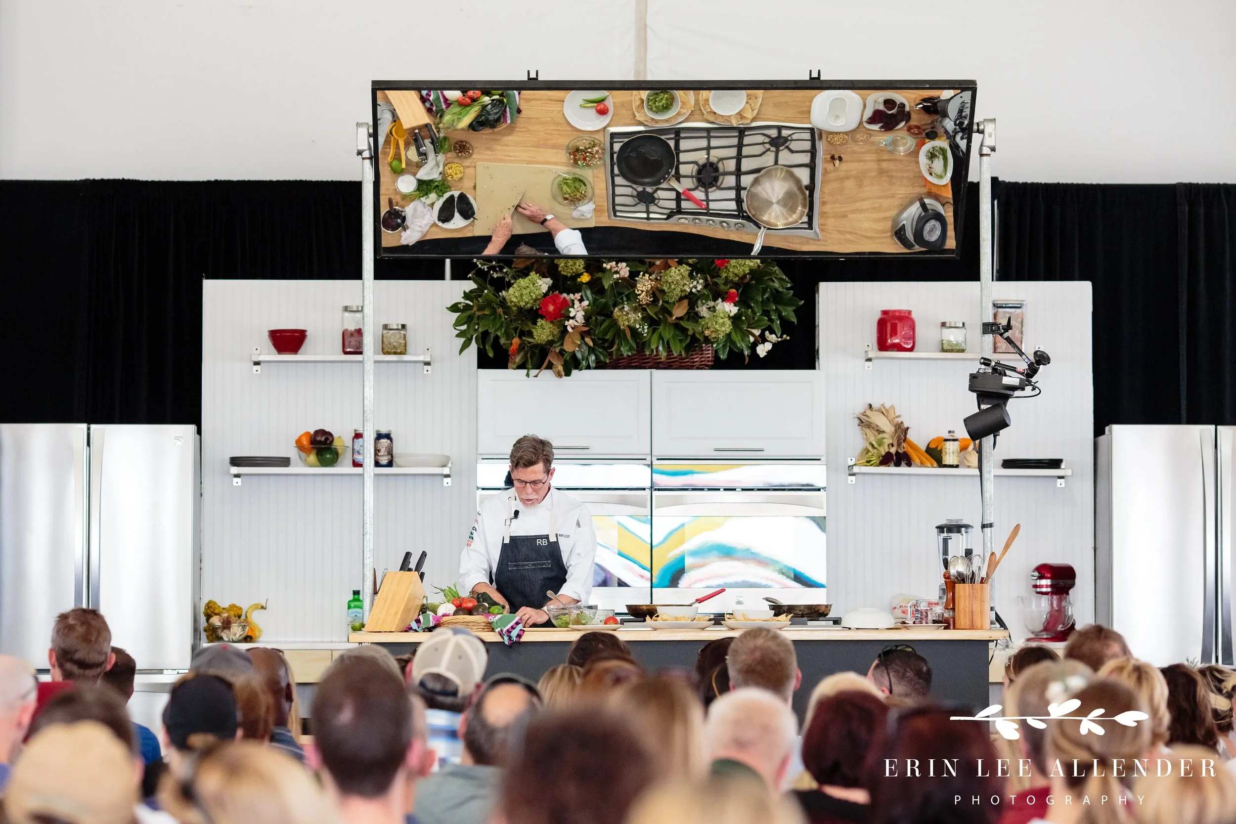 Wide shot of chef Rick Bayless presentation with mirror showing his cooking space to the crowd at the Music City Food and Wine Festival Nashville