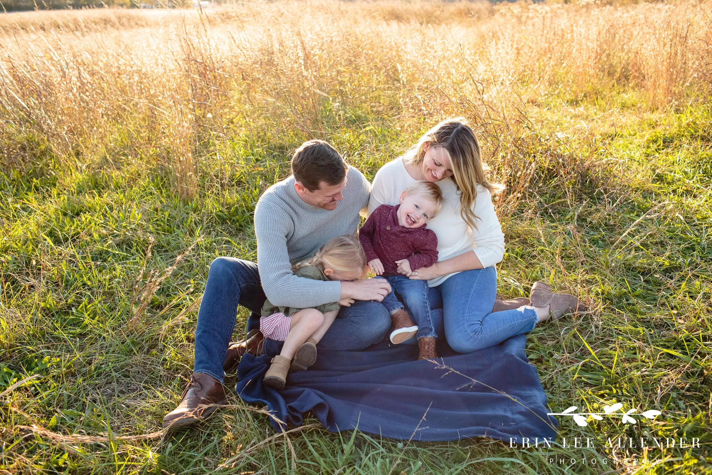 Family of four laughing and interacting naturally in a golden field during a Nashville family photography session.