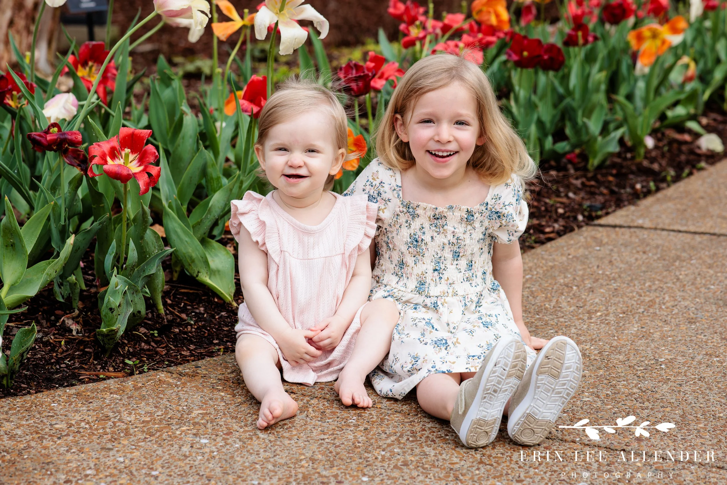 Two sisters sitting together among spring tulips at Cheekwood Botanical Garden during 1-year milestone session, photographed by Nashville family photographer