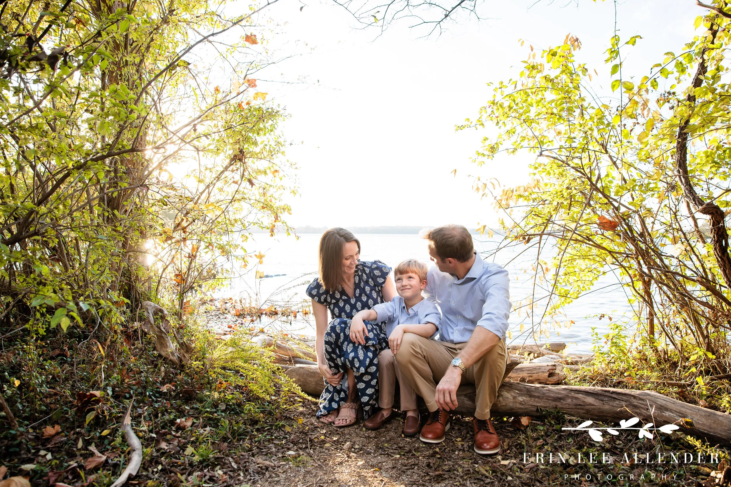 Nashville family photography — family of three sitting together on a log by the lake at Walton Ferry Arboretum in Hendersonville, TN, in soft late fall light