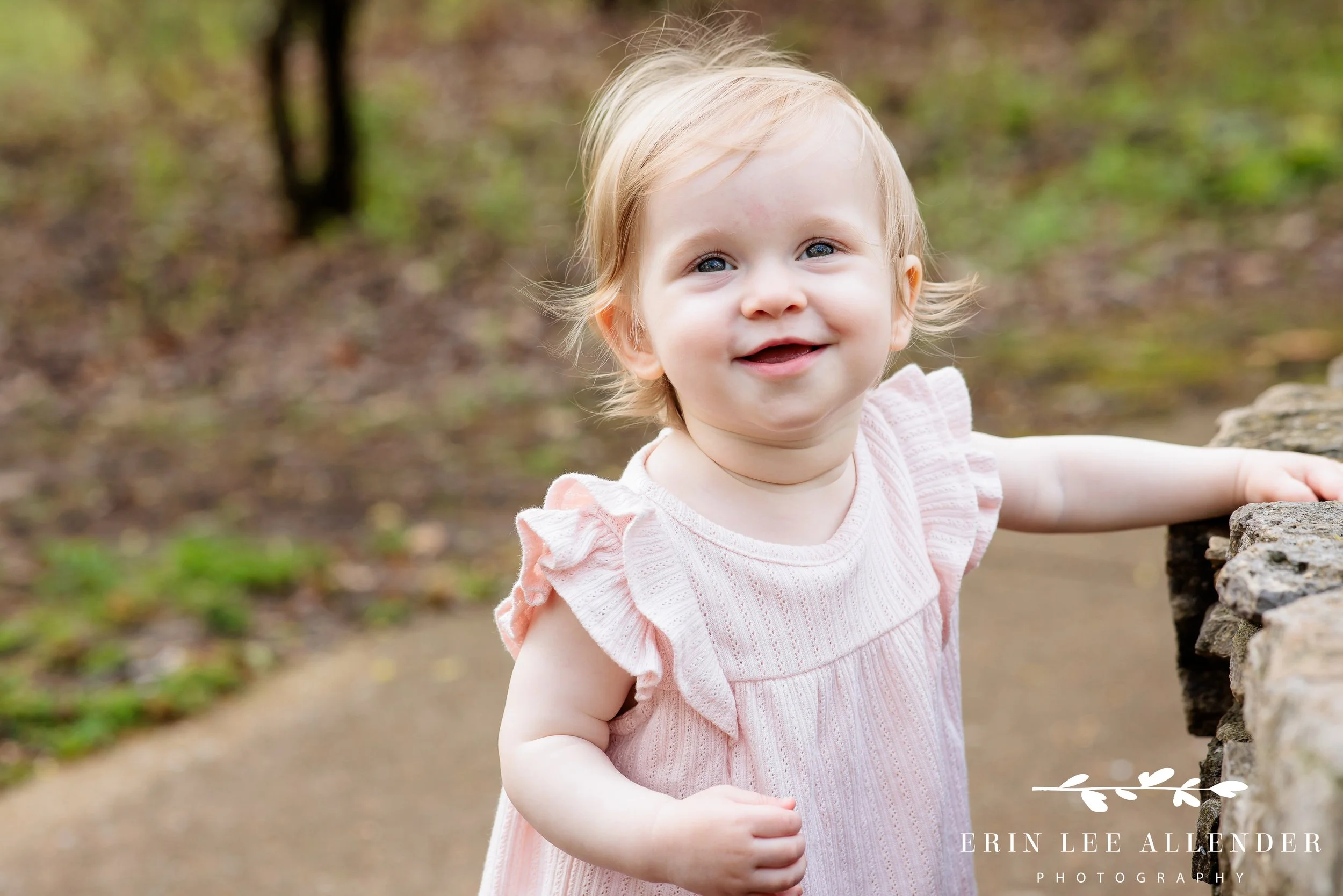 Toddler pulling up on wall and smiling during spring milestone session at Cheekwood Botanical Garden, Nashville family photographer