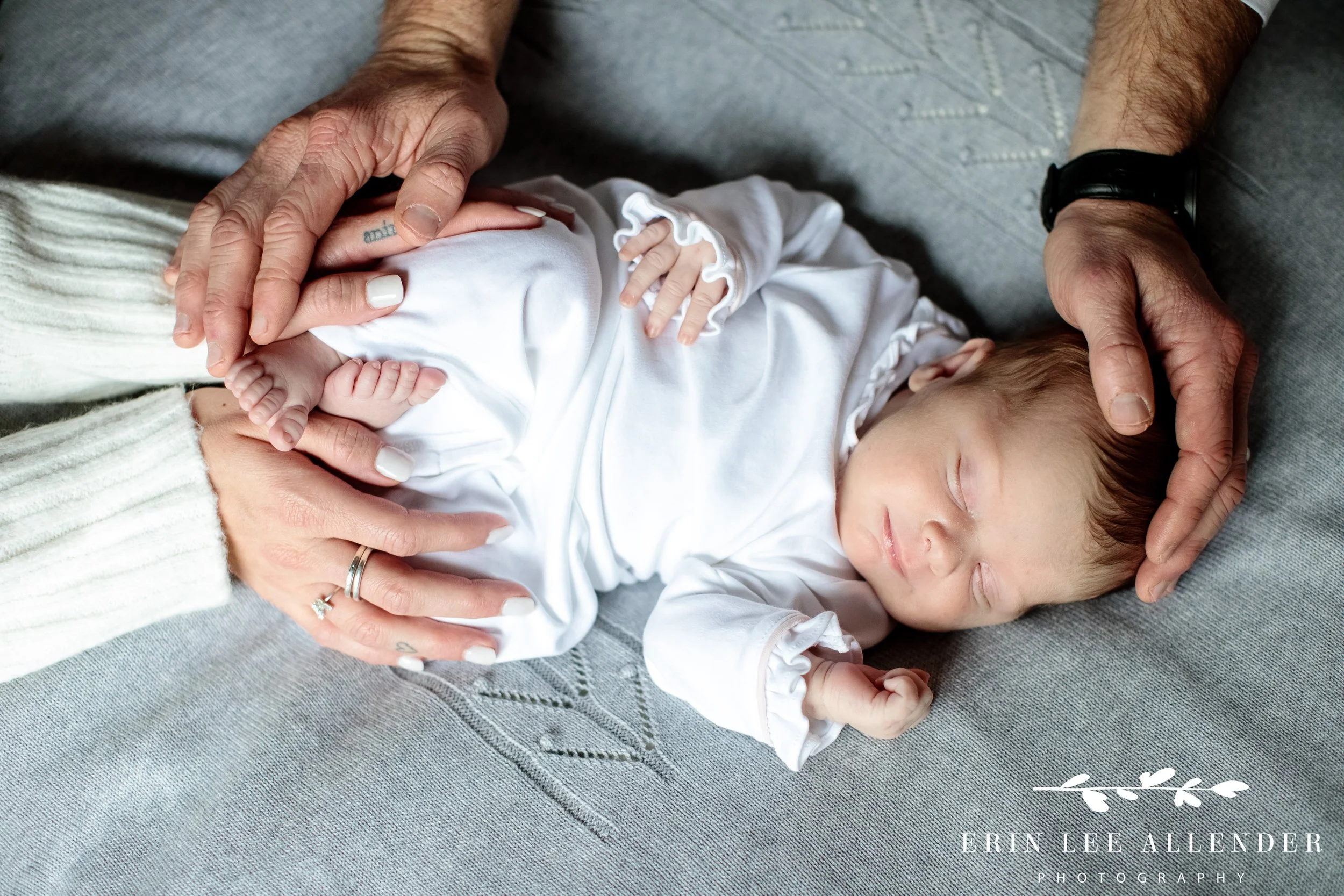 Close-up of mom and dad’s hands gently holding their newborn baby during an in-home session.