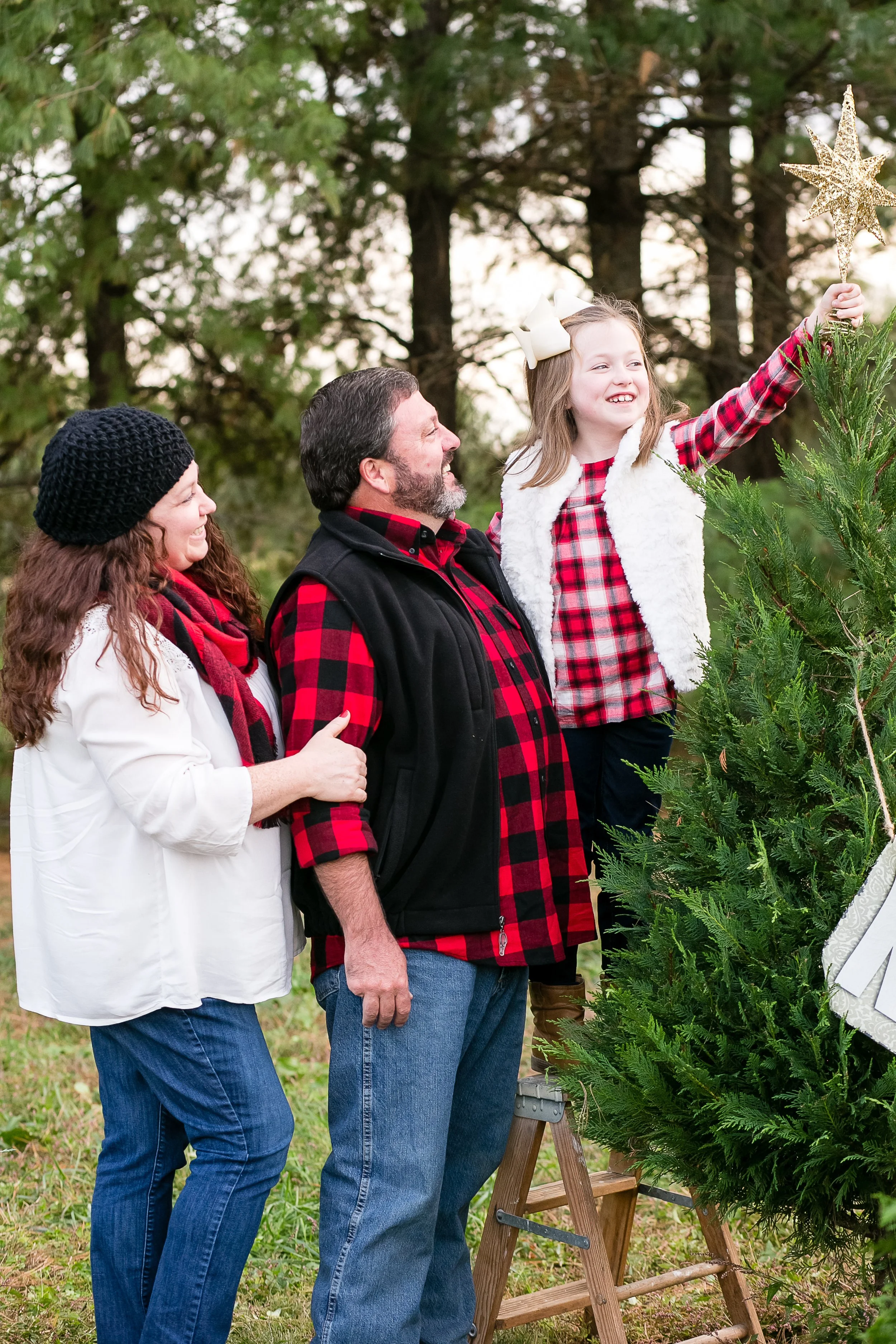 Young girl placing a star on a Christmas tree during a Nashville holiday mini session at Country Cove Christmas Tree Farm
