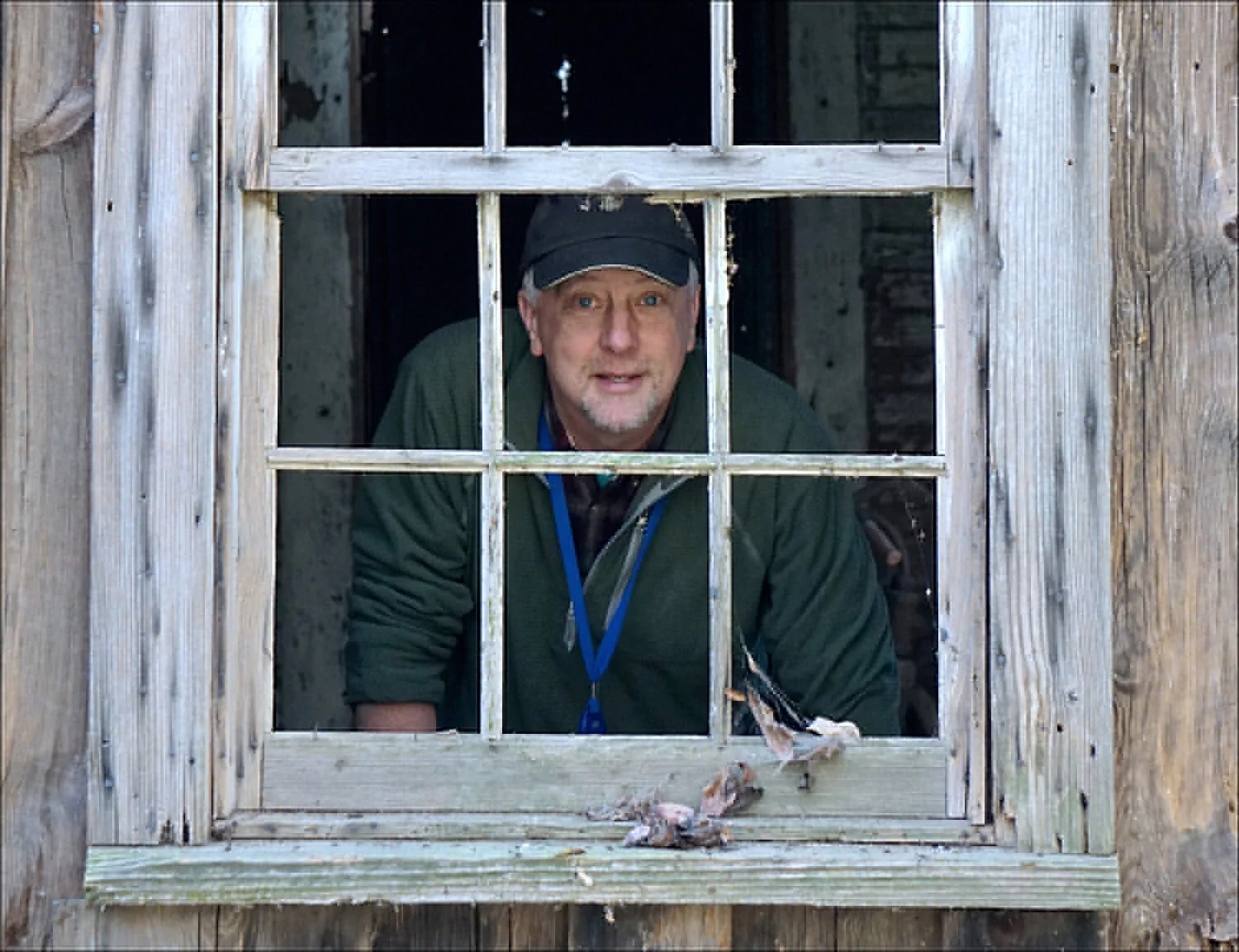 A man standing behind the window of an old wooden house.