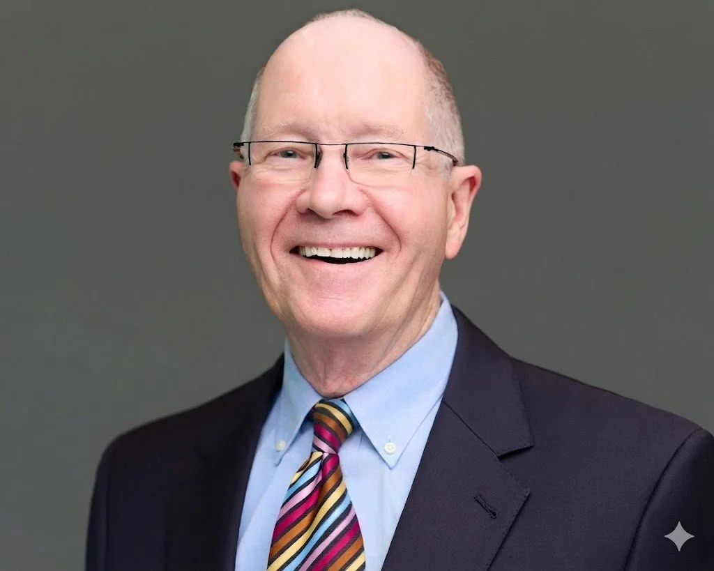 Headshot of a white man in a suit wearing wire-framed glasses