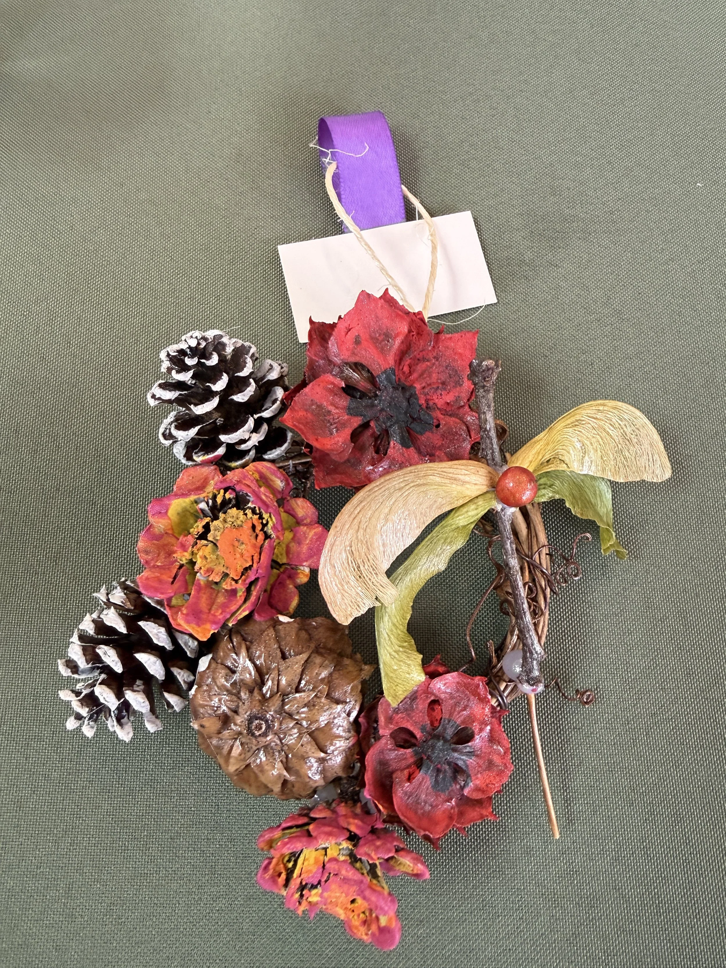 A small wreath made with natural materials such as pinecones and maple seeds pods.