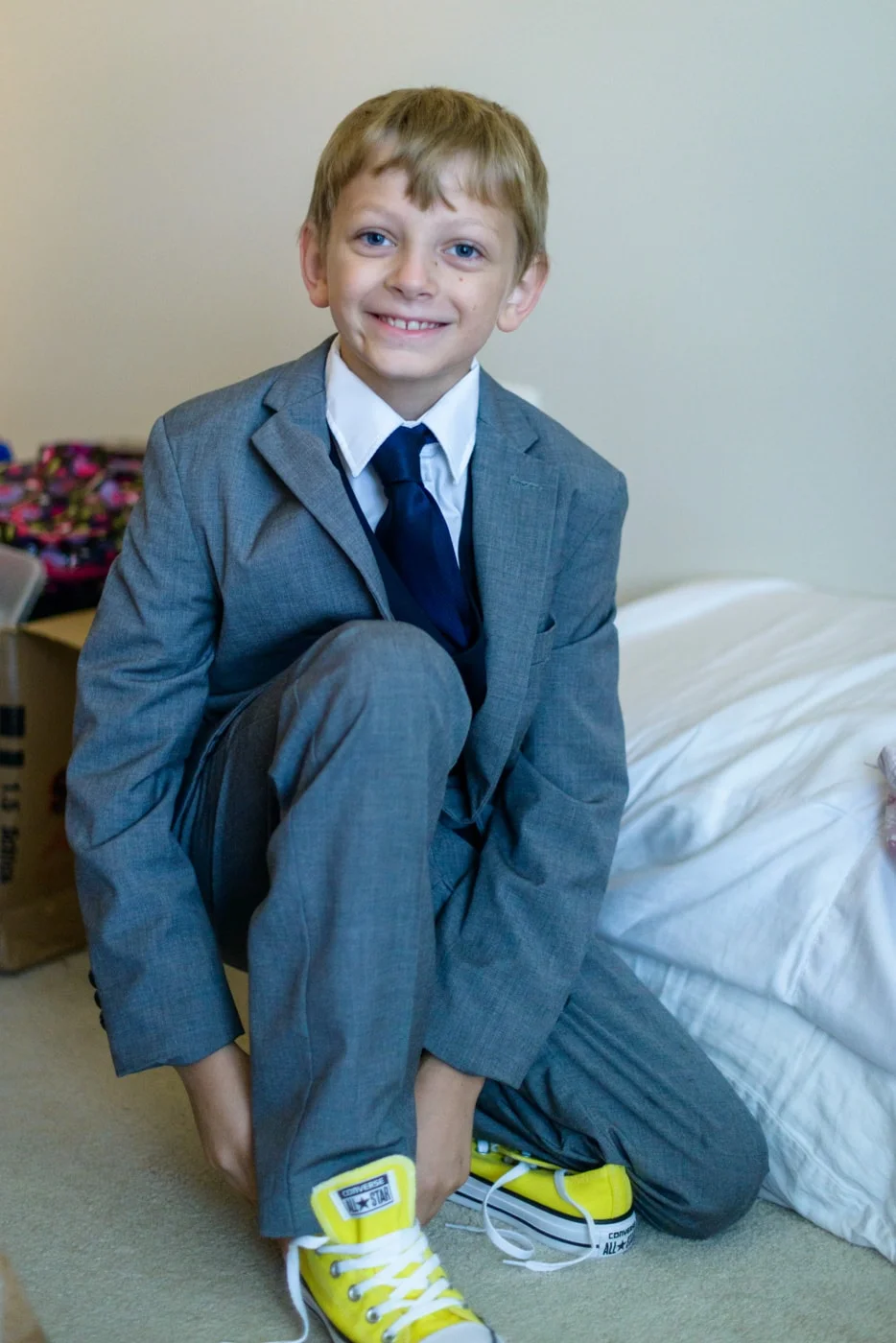 A young ring bearer puts on yellow sneakers with his suit before the wedding at a home in fairfax, virginia