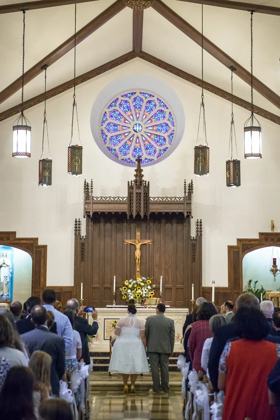 The bride and groom stand together facing the aisle at their wedding ceremony at St James Catholic Church in Falls Church, Virginia