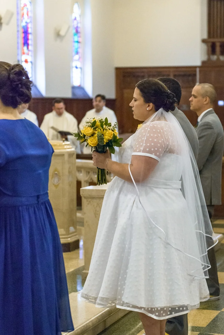 A prayerful bride and groom standing at the altar during their wedding ceremony at St James Catholic Church in Falls Church, Virginia