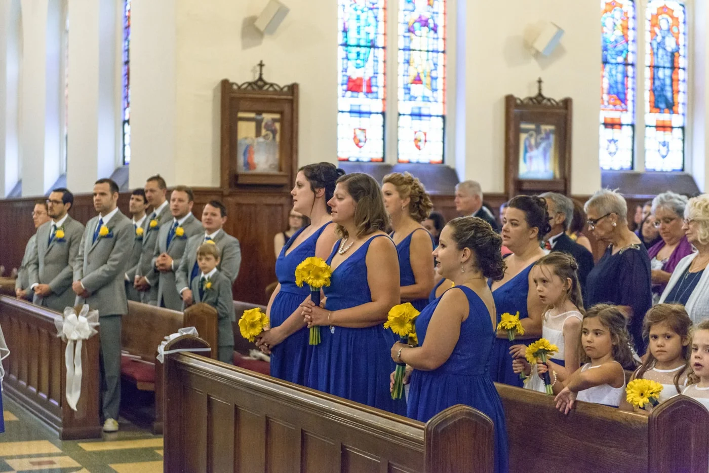 The wedding party standing in the pews during a wedding ceremony at St James Catholic Church in Falls Church, Virginia