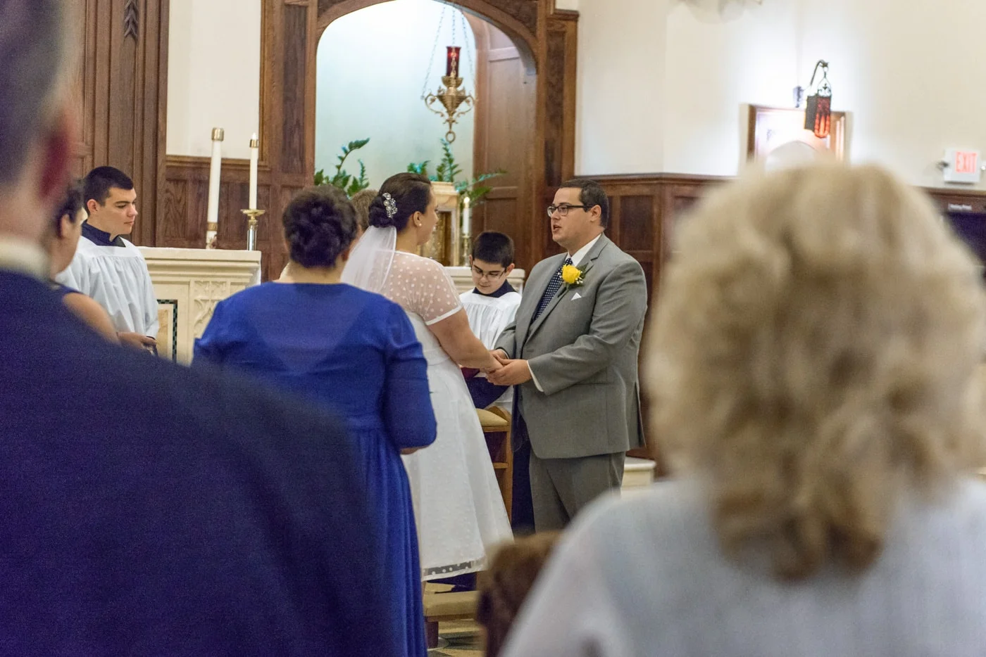 The bride and groom hold hands in front of the altar during their wedding ceremony at St James Catholic Church in Falls Church, Virginia
