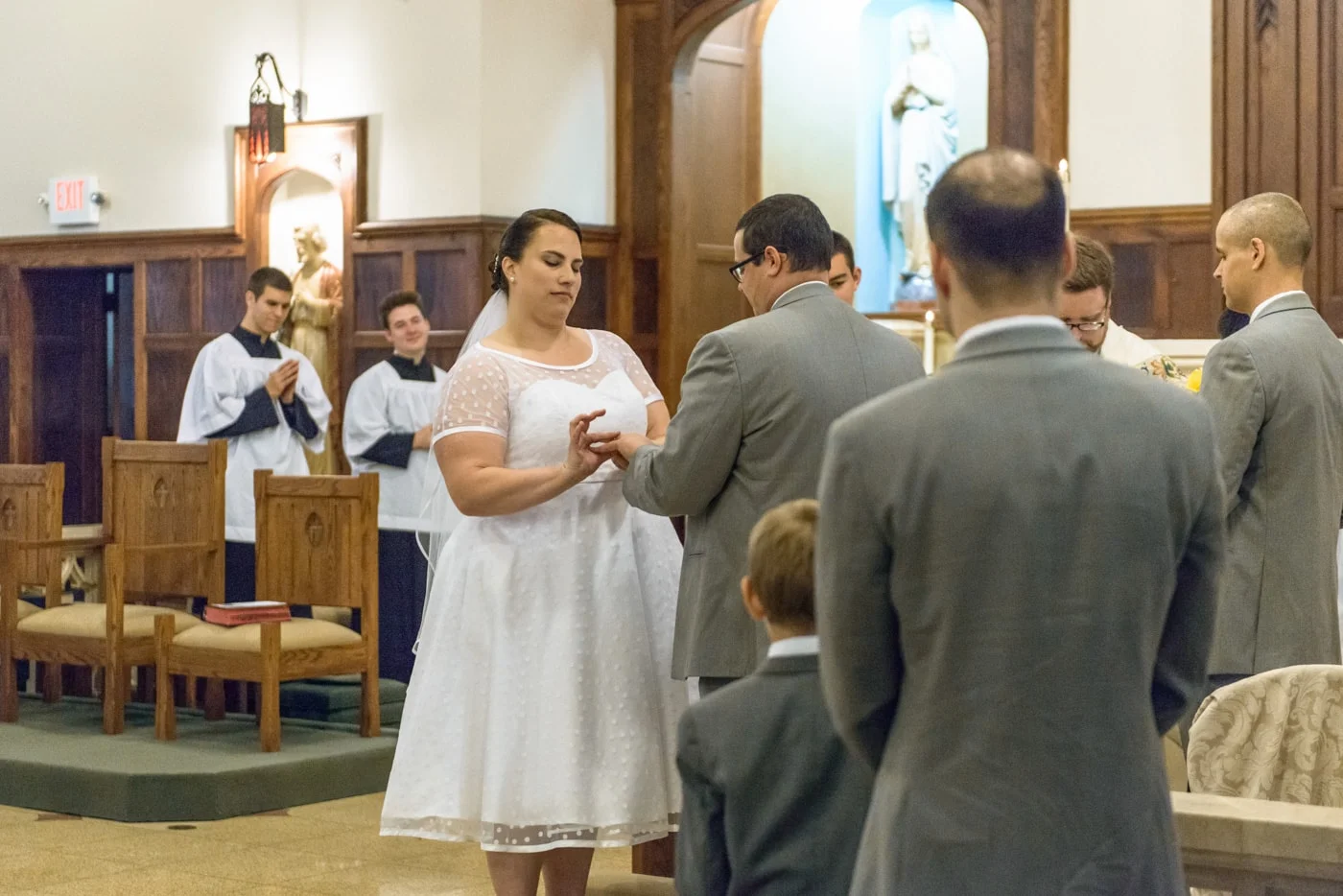 The bride puts the ring on the groom’s finger during exchanging of rings at wedding at St James Catholic Church in Fairfax, Virginia