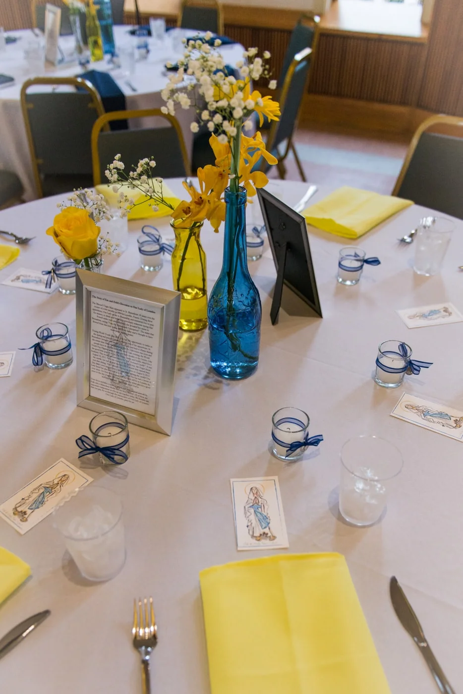 Detail of table settings with blue and yellow vases and candles at a brunch wedding reception at St Mark Catholic Church in Vienna, Virginia