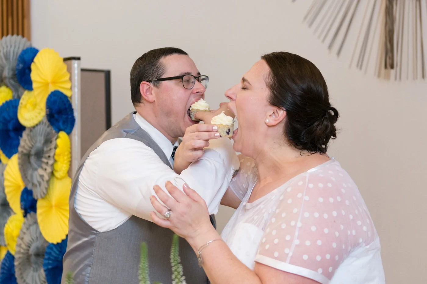 The bride and groom lock arms and eat cupcakes at their wedding reception at St Mark Catholic Church in Vienna, Virginia