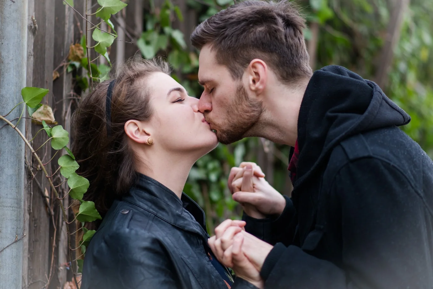 A young couple hold hands and kiss as she leans against a fence in old town alexandria