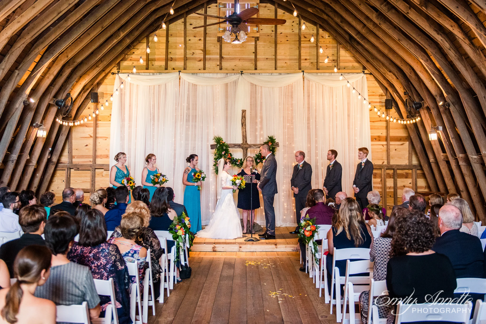 A bride and groom stand with the wedding party and an officiant inside a decorated barn for a wedding ceremony during a country wedding at Amber Grove near Richmond, Virginia