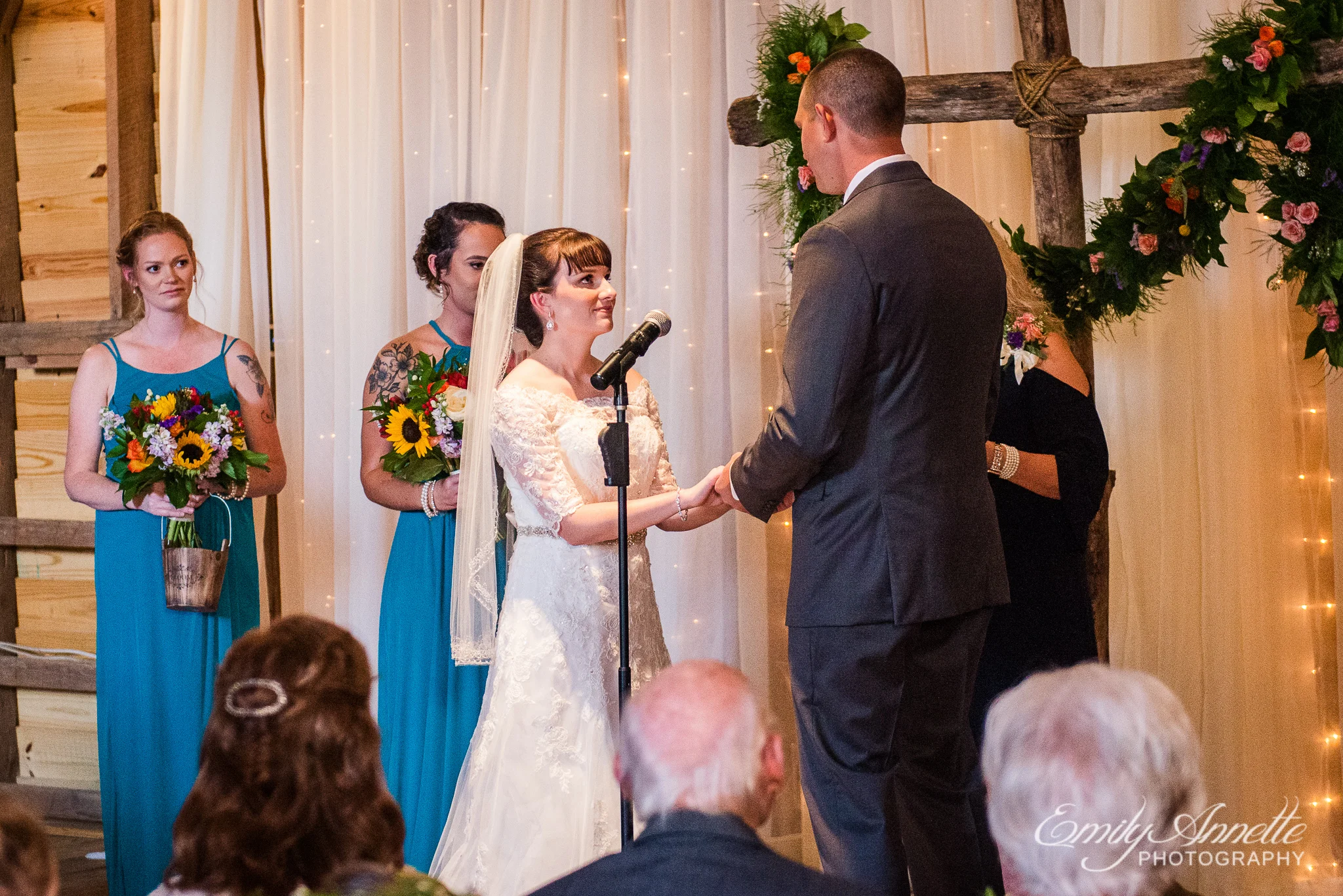 The bride and groom hold hands at the altar inside a decorated barn for a wedding ceremony during a country wedding at Amber Grove near Richmond, Virginia