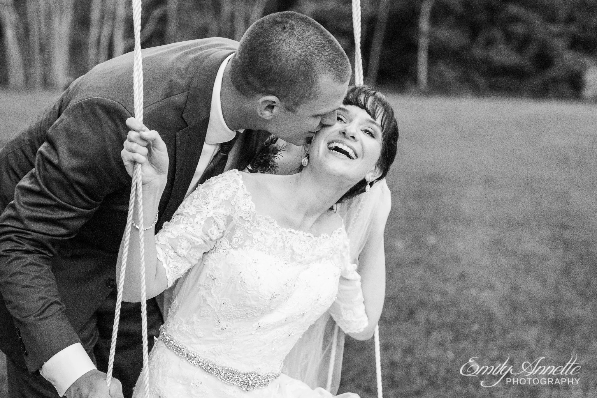 A groom kisses his bride while she sits on a swing hanging from a tree after their country wedding at Amber Grove near Richmond, Virginia