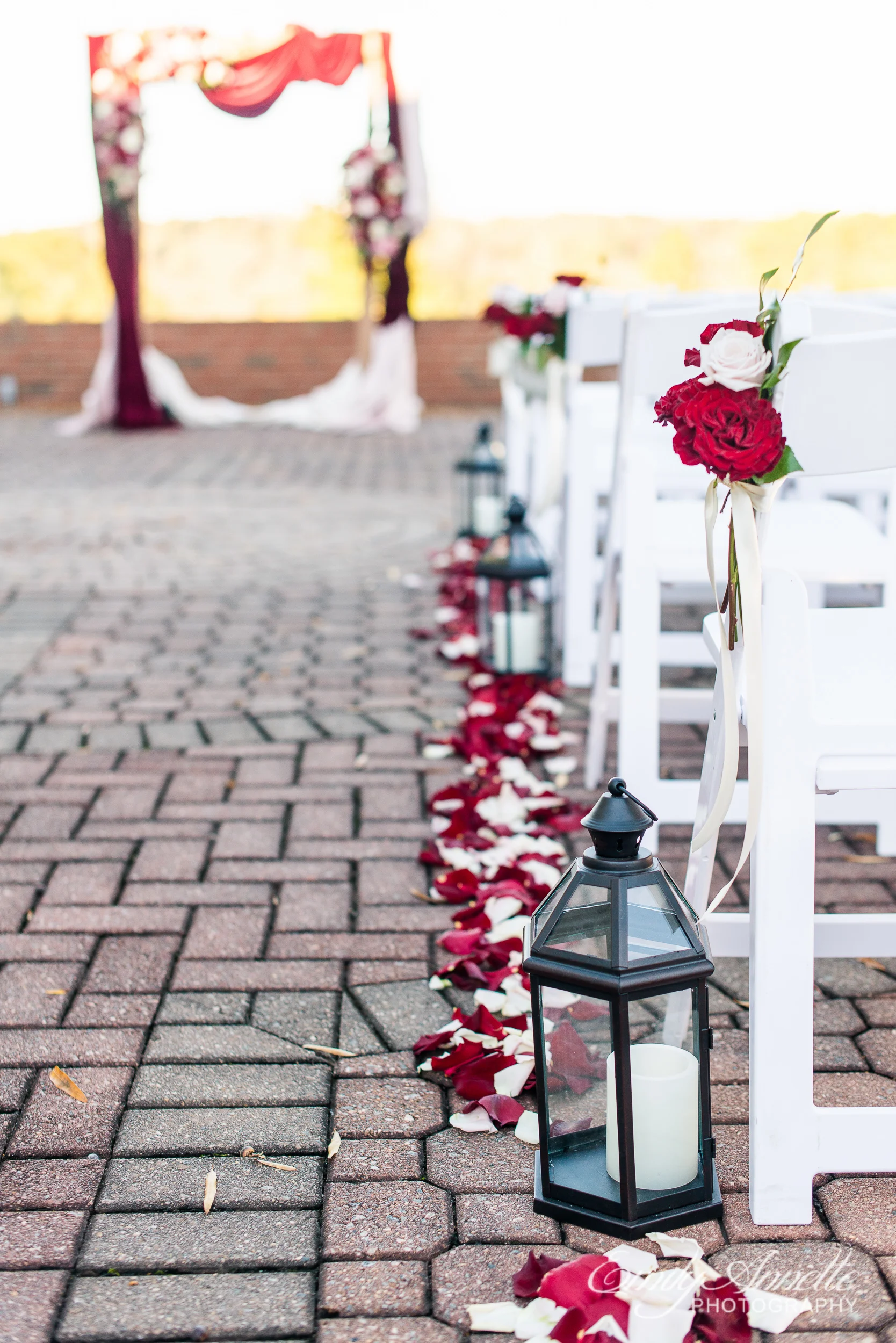 Ceremony site decorations including lanterns, rose petals, and flower bouquets on chairs at Willow Oaks Country Club in Richmond, Virginia