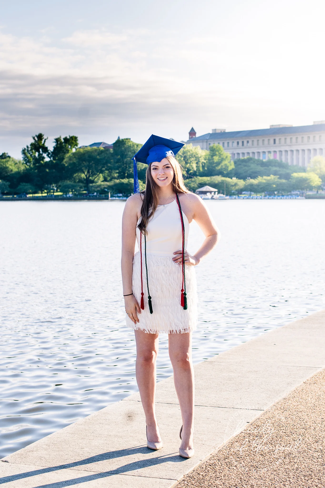 A graduate from Marymount University in Arlington, Northern Virginia standing beside the Potomac River by the Tidal Basin for her cap and gown session in Washington, DC