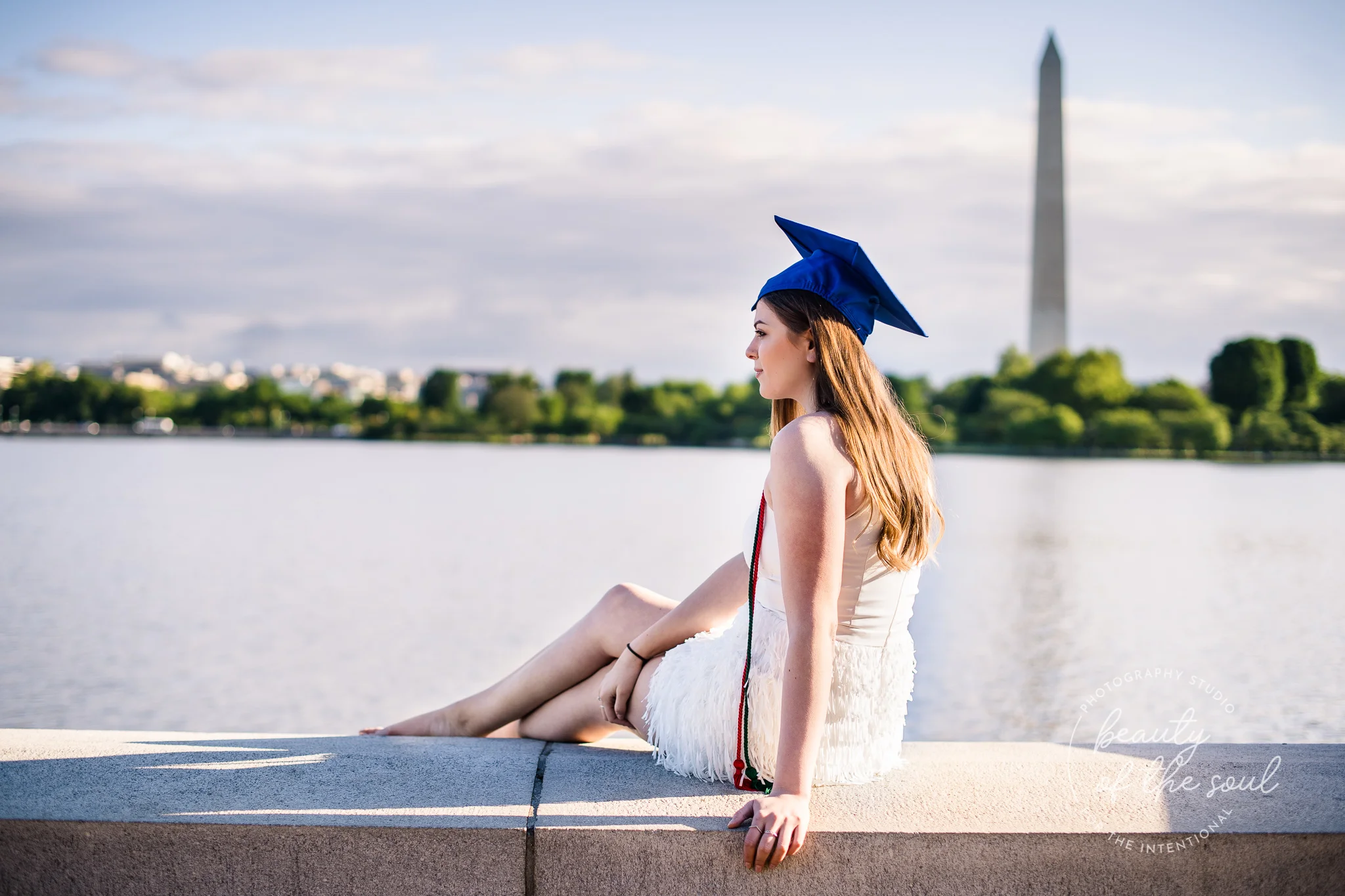A graduate from Marymount University in Arlington, Northern Virginia sitting beside the Potomac River at the Tidal Basin for her cap and gown session in Washington, DC