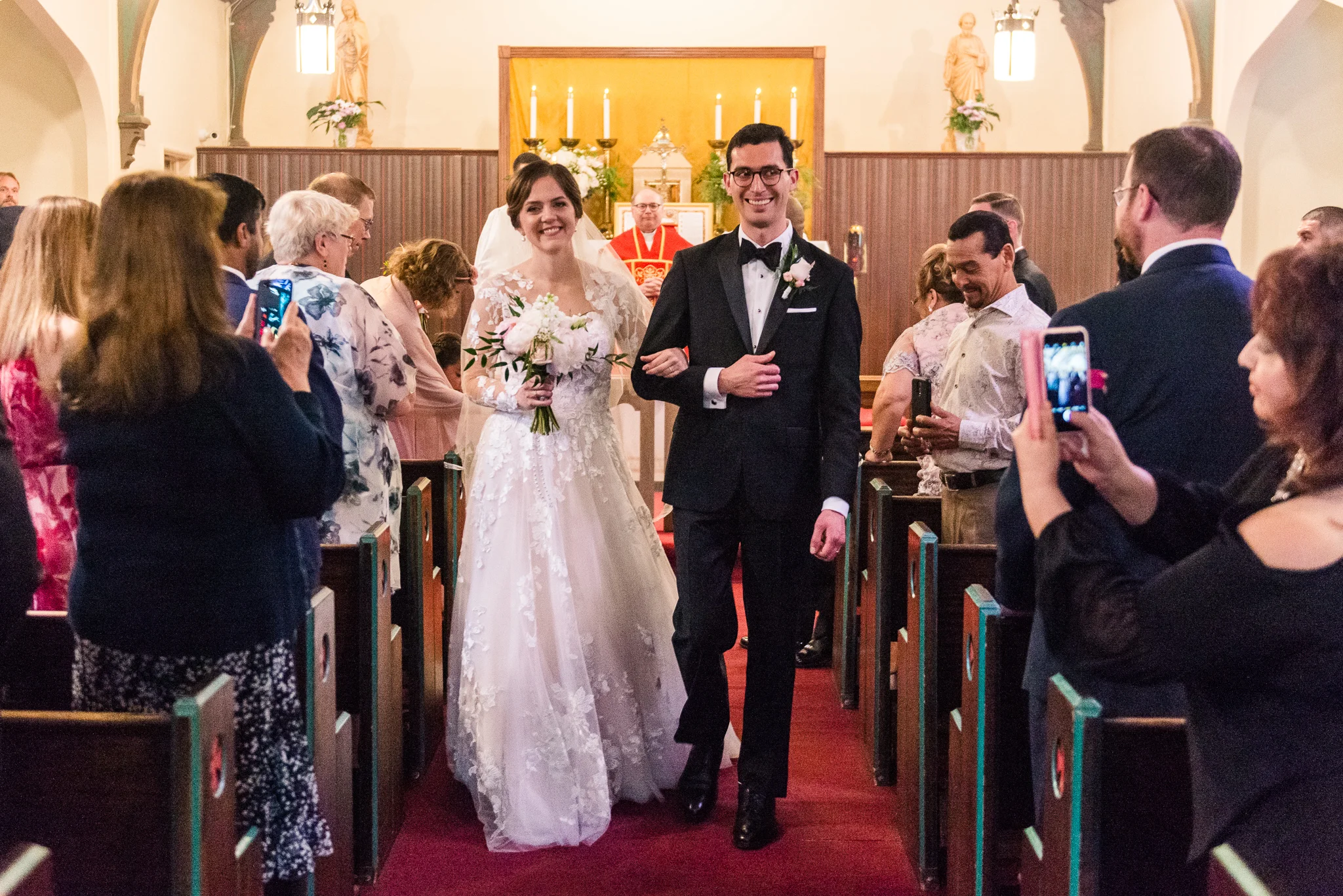 A bride and groom recess joyfully arm in arm after a Catholic wedding ceremony at the Chapel of Immaculate Conception in Leesburg, Northern Virginia
