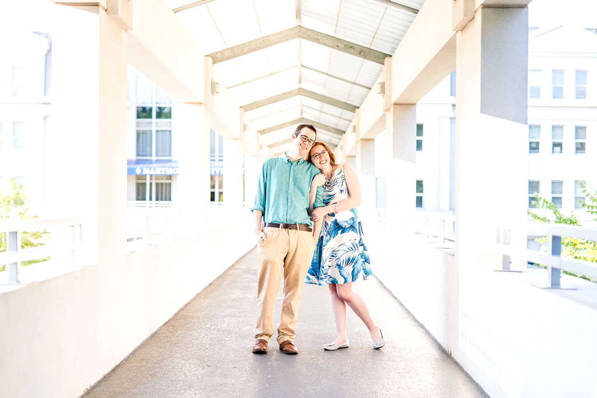 An engaged couple snuggle in together while standing on the bridge to Ostapenko Hall at Marymount University during their summer sunrise engagement session in Arlington, Northern Virginia