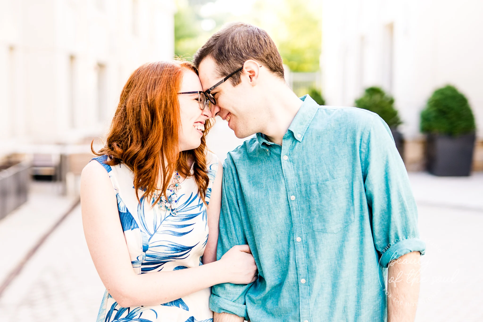 An engaged couple laughs together as they stand in Malek Plaza at Marymount University during their summer sunrise engagement session in Arlington, Northern Virginia