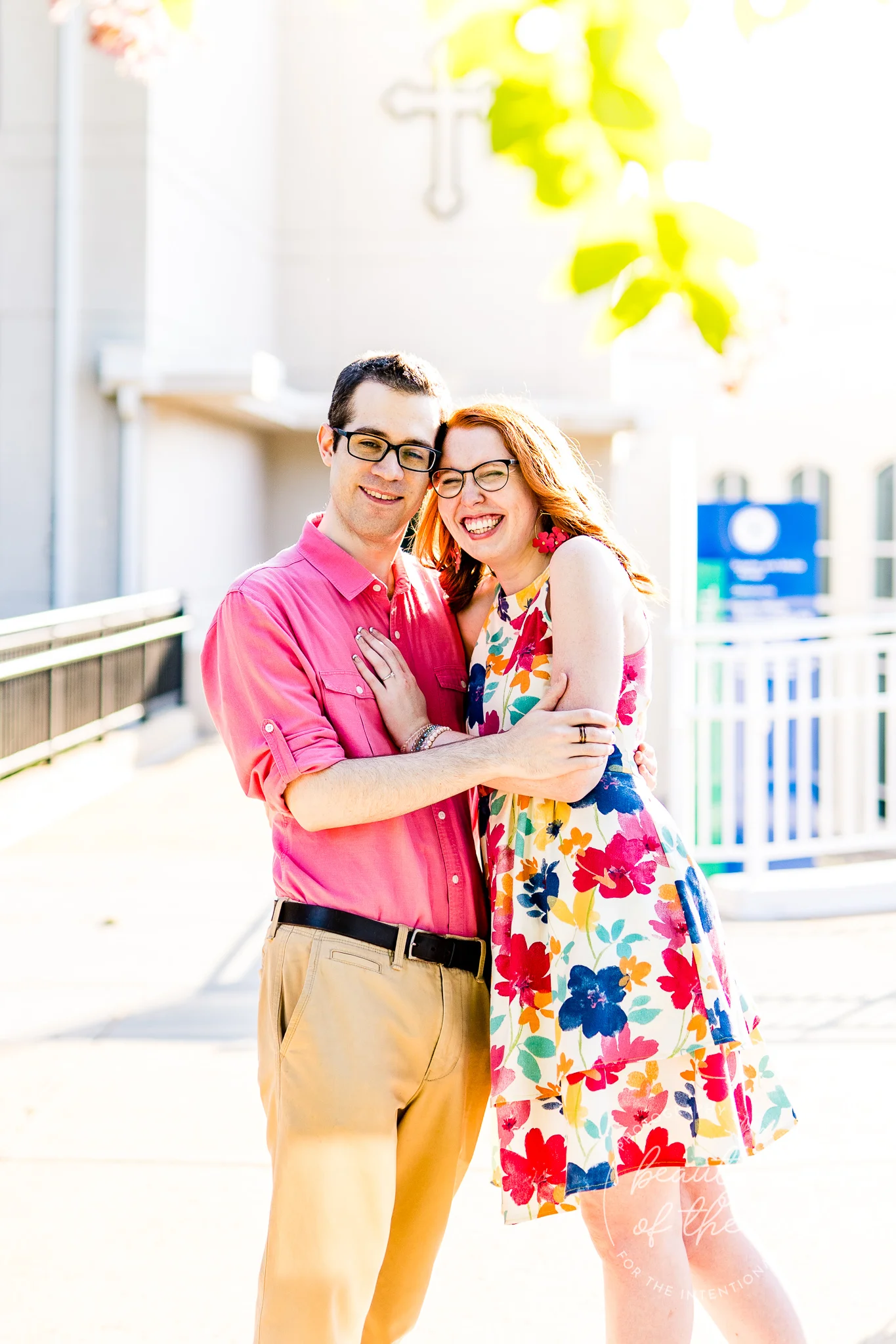 An engaged couple stand and smile together in front of Gailhac Hall at Marymount University during their summer sunrise engagement session in Arlington, Northern Virginia